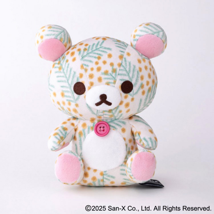 【商品写真】キッピスミモザ柄をまとった、お座りしているコリラックマのぬいぐるみ。耳や手足はピンクで、胸には赤いボタンがついています