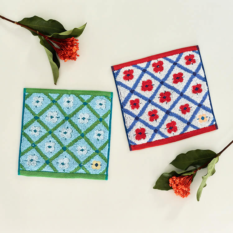 【商品写真】少しレトロさの漂う花柄「
						Lotta」がデザインされている正方形のタオルハンカチ。白い生地に赤色の花柄と青紫色の格子柄がデザインされていて、右下にはベージュの花がワンポイントで施されています